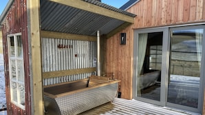 Uma cabana de madeira com sauna, um banco de metal e uma porta de correr de vidro que dá para uma área externa coberta.