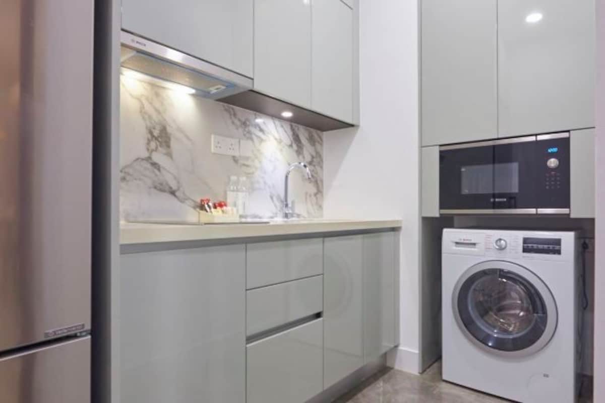 A compact kitchen with a built-in washing machine, a microwave, and a stainless steel refrigerator.