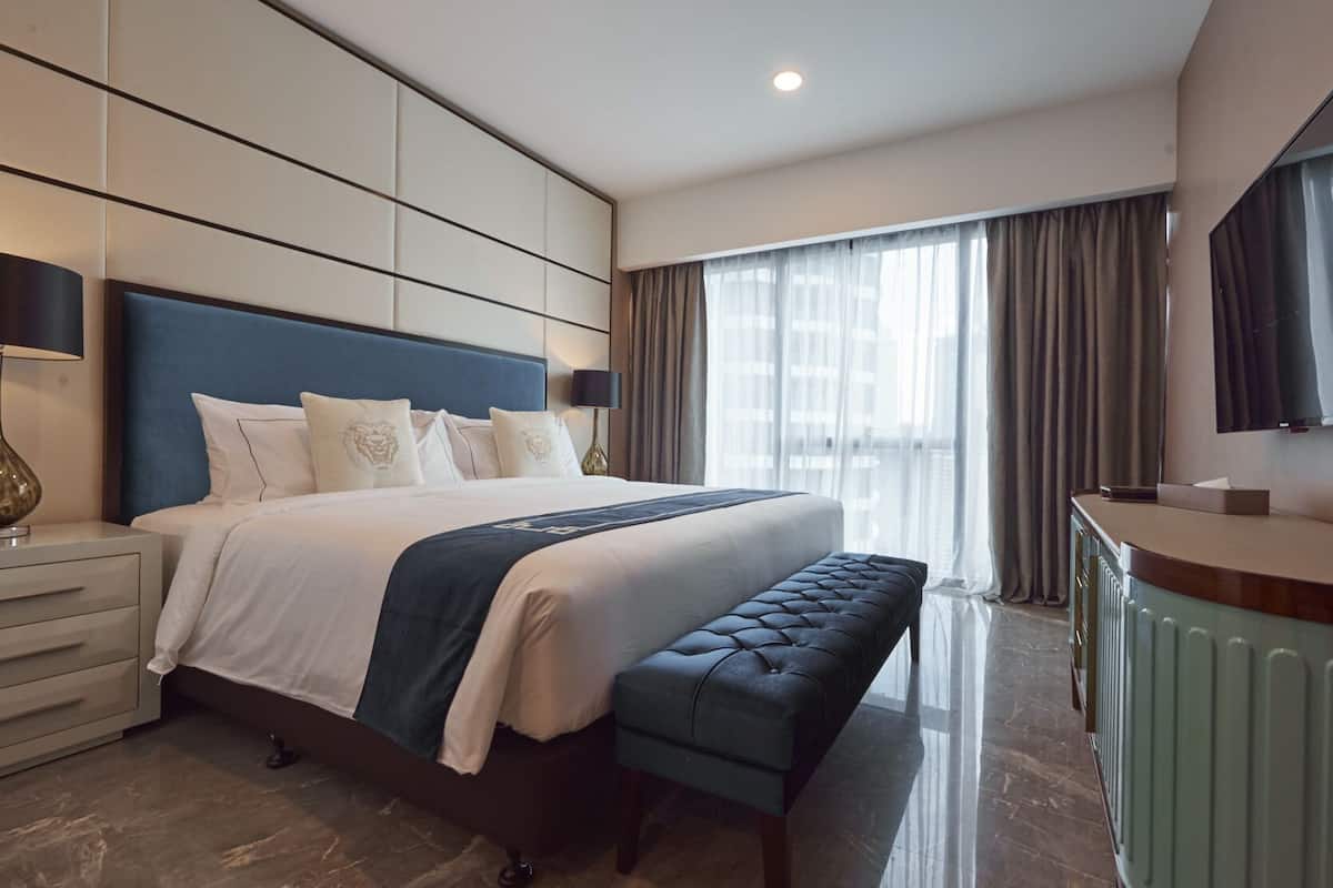 A modern hotel room with a large bed, a bench, a desk, and a TV.