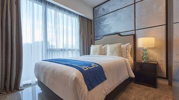 A hotel room with a large bed, a headboard with a geometric pattern, a nightstand with a lamp, and a view through sheer curtains.