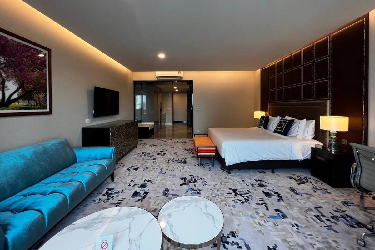 A hotel room with a bed, a sofa, a coffee table, a TV, and a patterned carpet.