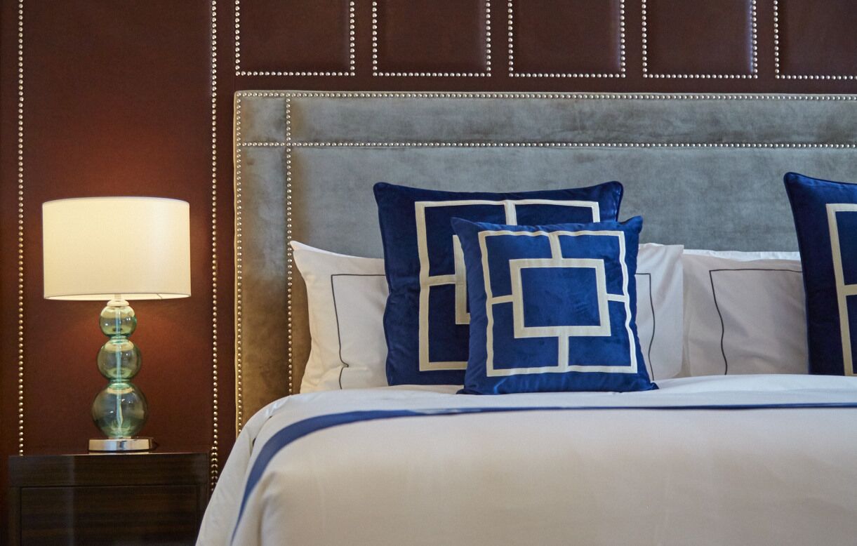 Une chambre d’hôtel avec une tête de lit capitonnée, une lampe de chevet et des oreillers à motifs bleus et blancs.