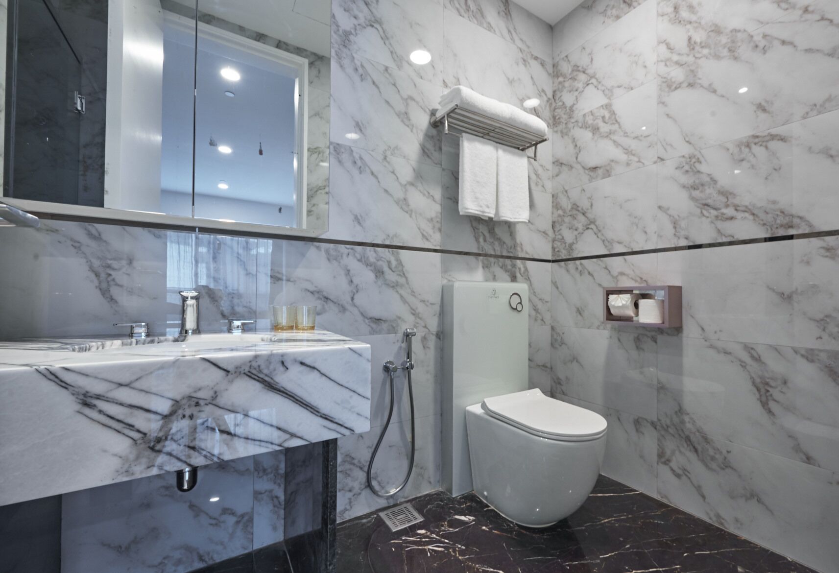 A modern bathroom with a marble vanity, a glass shower enclosure, and a toilet.