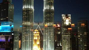 A nighttime cityscape with two prominent skyscrapers, a large building with a unique triangular structure, and a circular water feature.