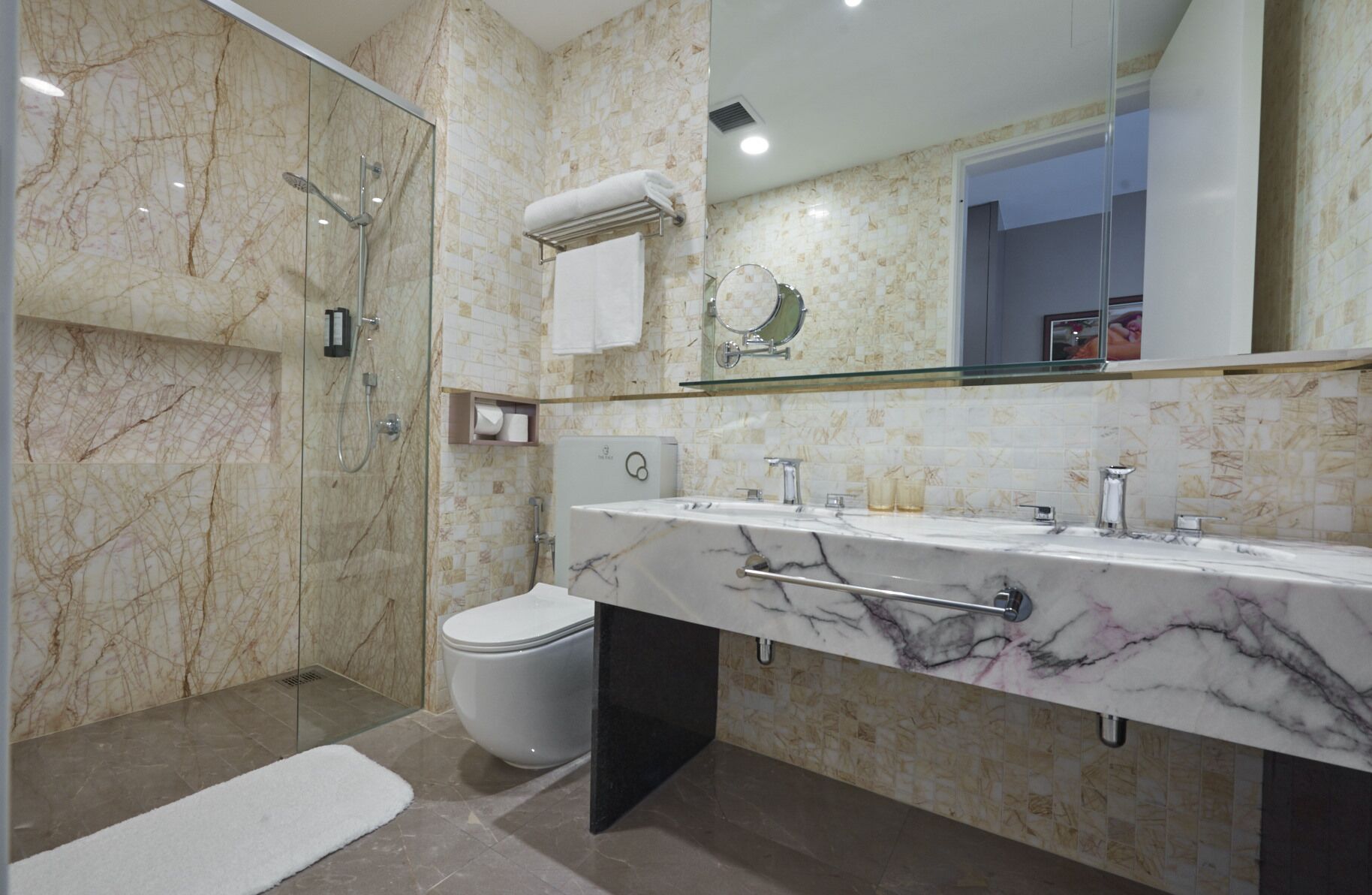 Une salle de bain moderne avec une douche à parois de verre, des toilettes et un meuble-lavabo en marbre agrémenté d’un grand miroir.