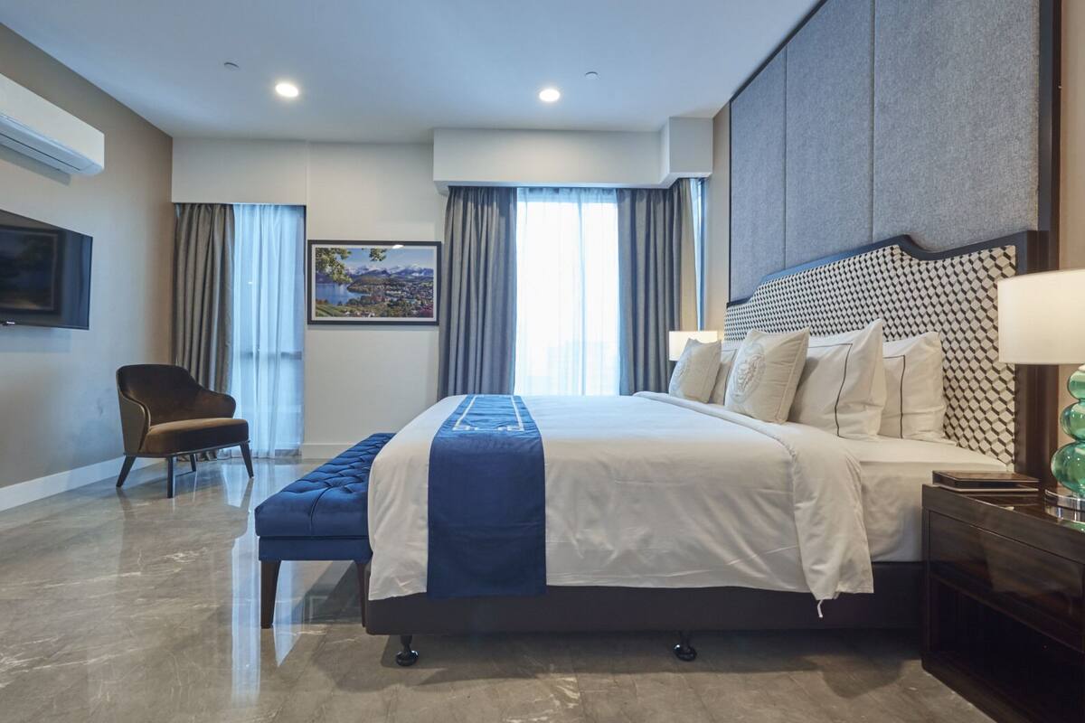 A modern hotel room with a large bed, a chair, a desk, and a TV.