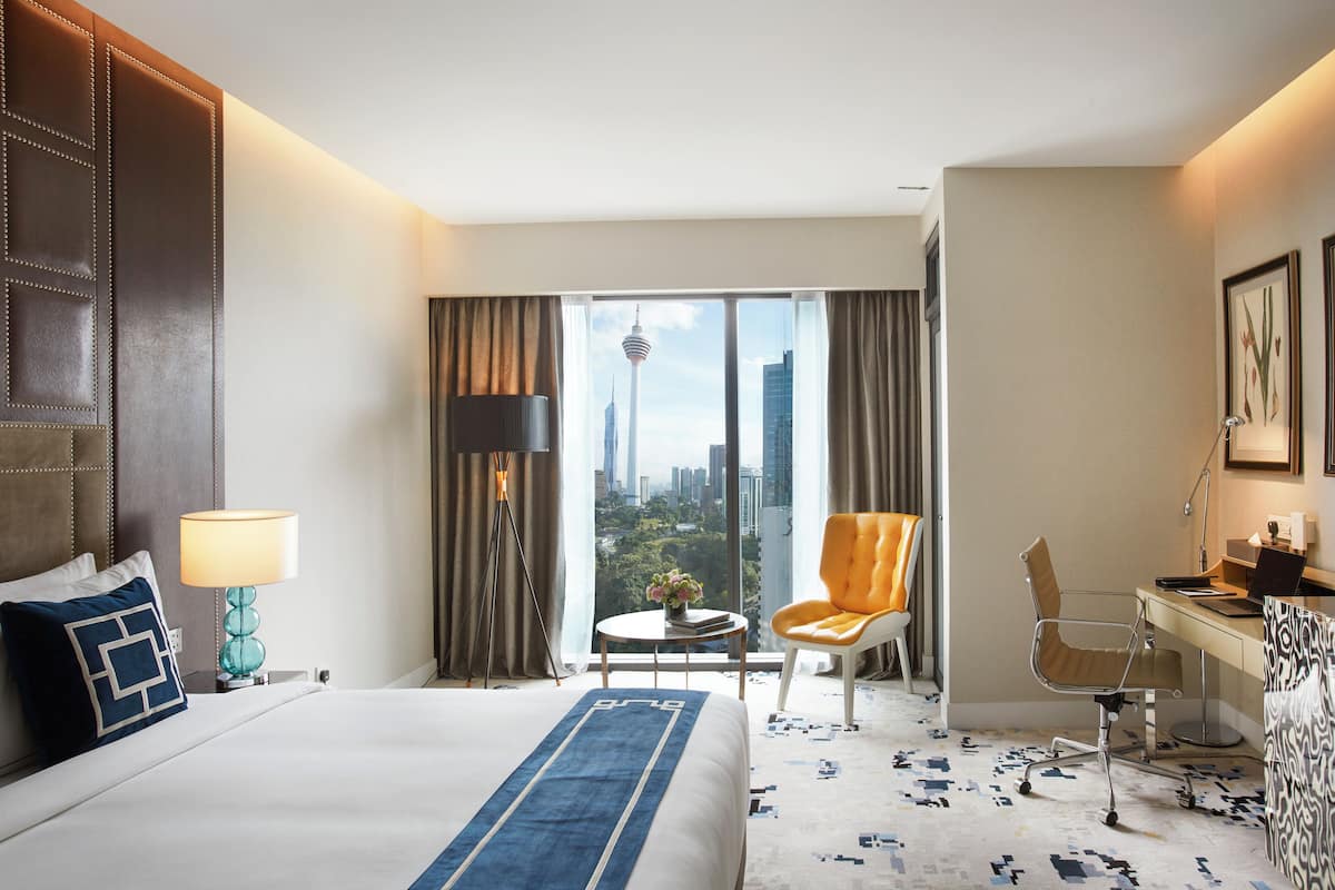 A hotel room with a large bed, a desk, a chair, and a view of a cityscape.