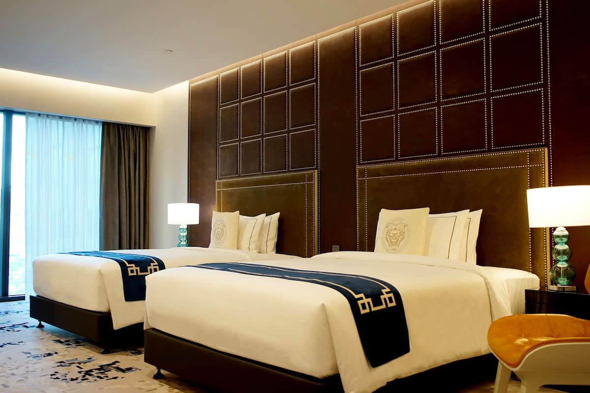 A hotel room with two beds, a large padded headboard, a view of the city, and a modern lamp.