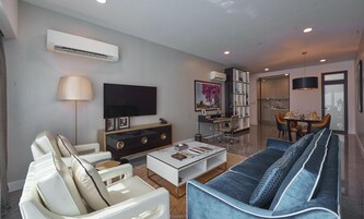 A modern living room with a flat-screen TV, a sofa, a coffee table, and a dining area with chairs and a table.