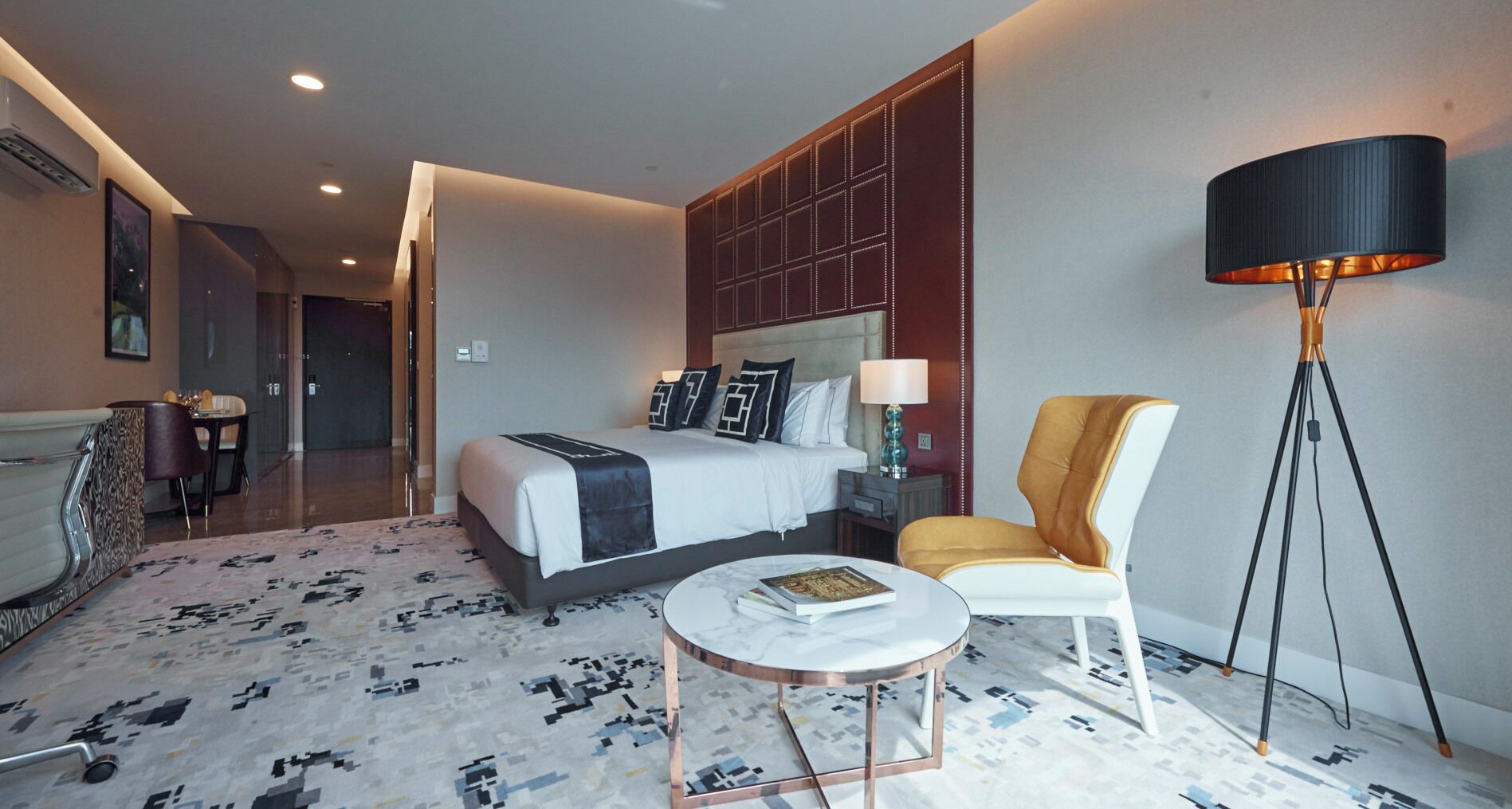 A modern hotel room with a large bed, a sitting area with a chair, a small table, and a floor lamp.