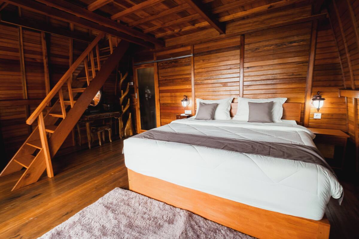A wooden cabin bedroom with a bed, a wooden ladder, and two wall-mounted lamps.