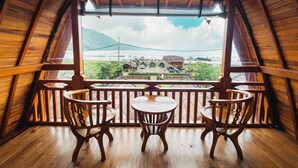 Un balcón de madera con dos sillas y una mesa, con vistas a un pueblo de edificios tradicionales y una montaña al fondo.