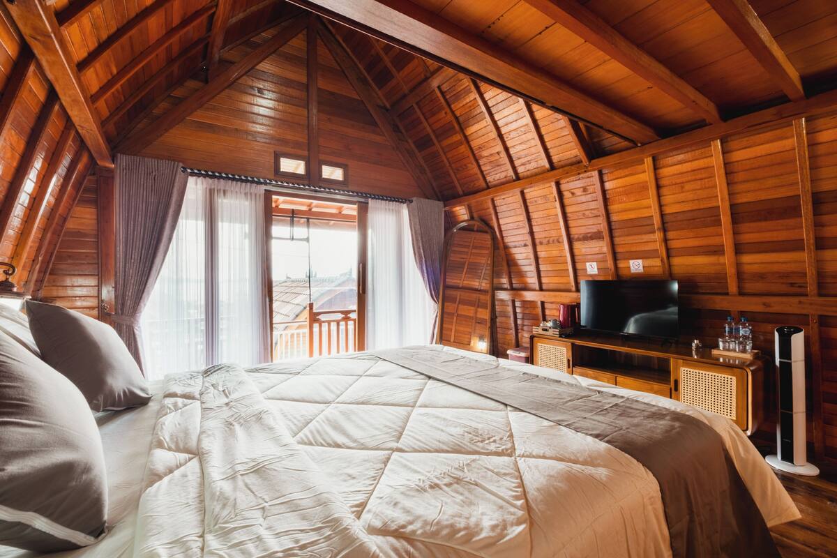 A wooden-paneled bedroom with a large bed, a television, and a view through a window.