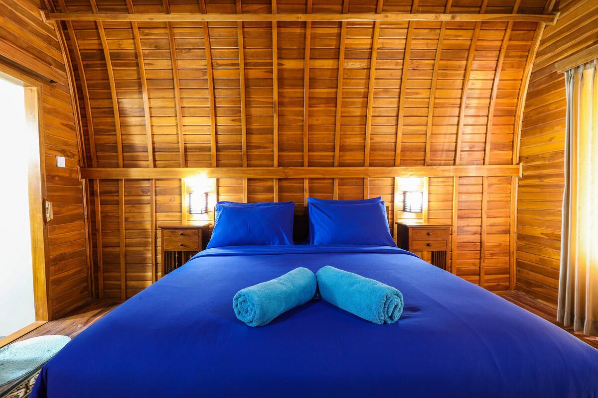 A wooden-paneled room with a bed, two nightstands, and a window.