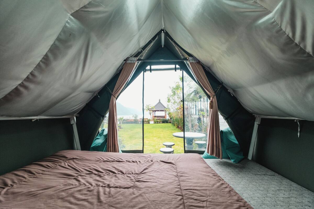 A tented room with a bed, a view of a garden, and a gazebo in the distance.