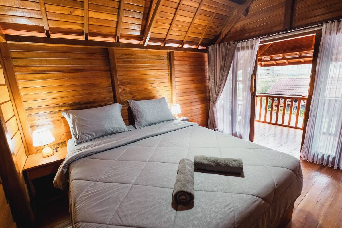 A wooden-paneled bedroom with a bed, pillows, a nightstand, and a window with curtains.