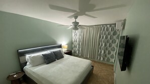 A bedroom with a bed, a ceiling fan, a nightstand with a lamp, and a TV mounted on the wall. - Beach Getaway (Punta Santiago ,Humacao)