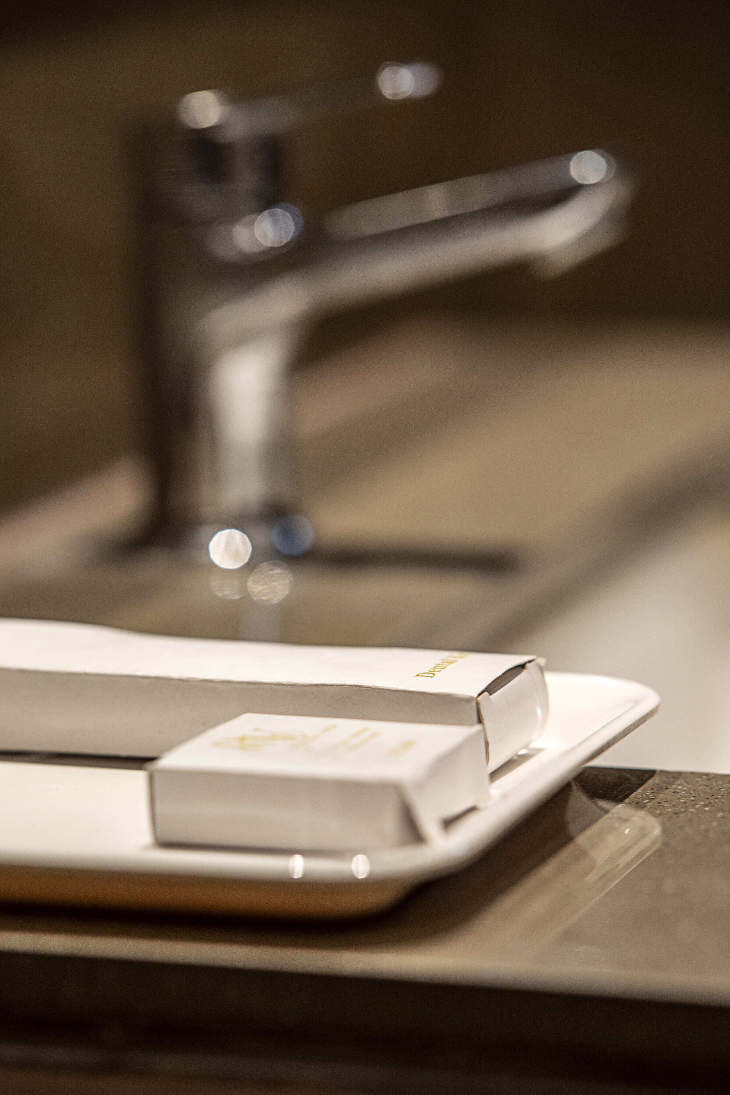A bathroom sink with a modern faucet and a soap dispenser on a white tray.