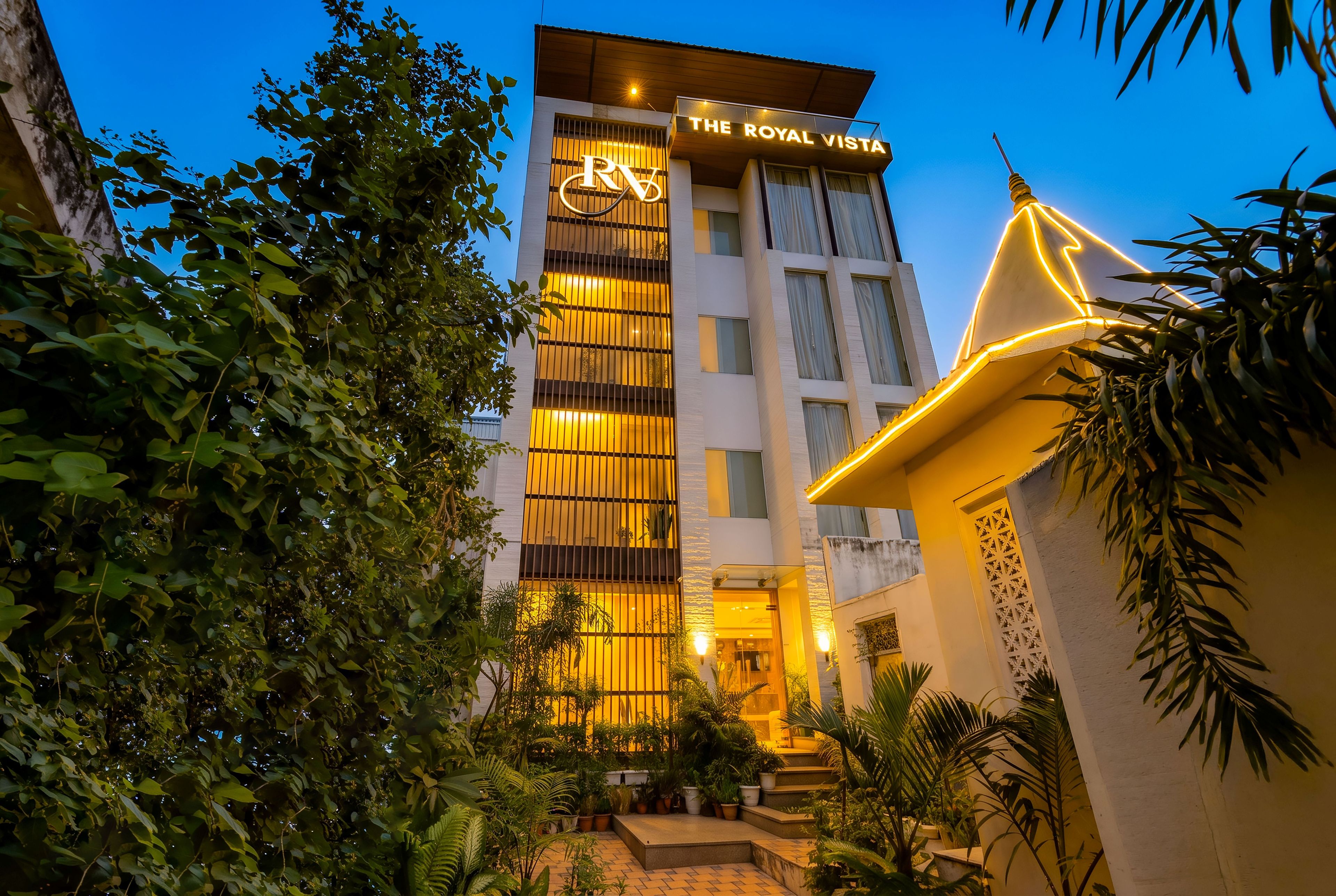 Un hotel llamado 'The Royal Vista' con una fachada moderna, grandes ventanales y una entrada bien iluminada.