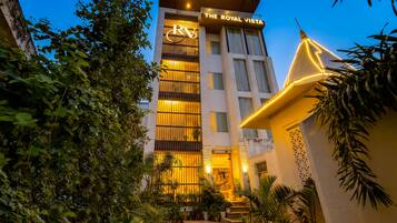 Un hotel llamado 'The Royal Vista' con una fachada moderna, grandes ventanales y una entrada bien iluminada.
