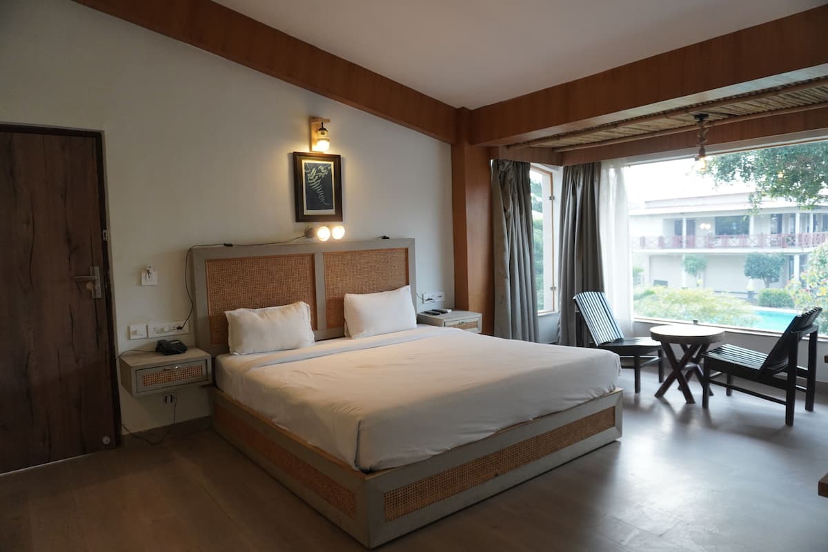 A hotel room with a large bed, bedside tables, a desk with chairs, and a window with curtains.