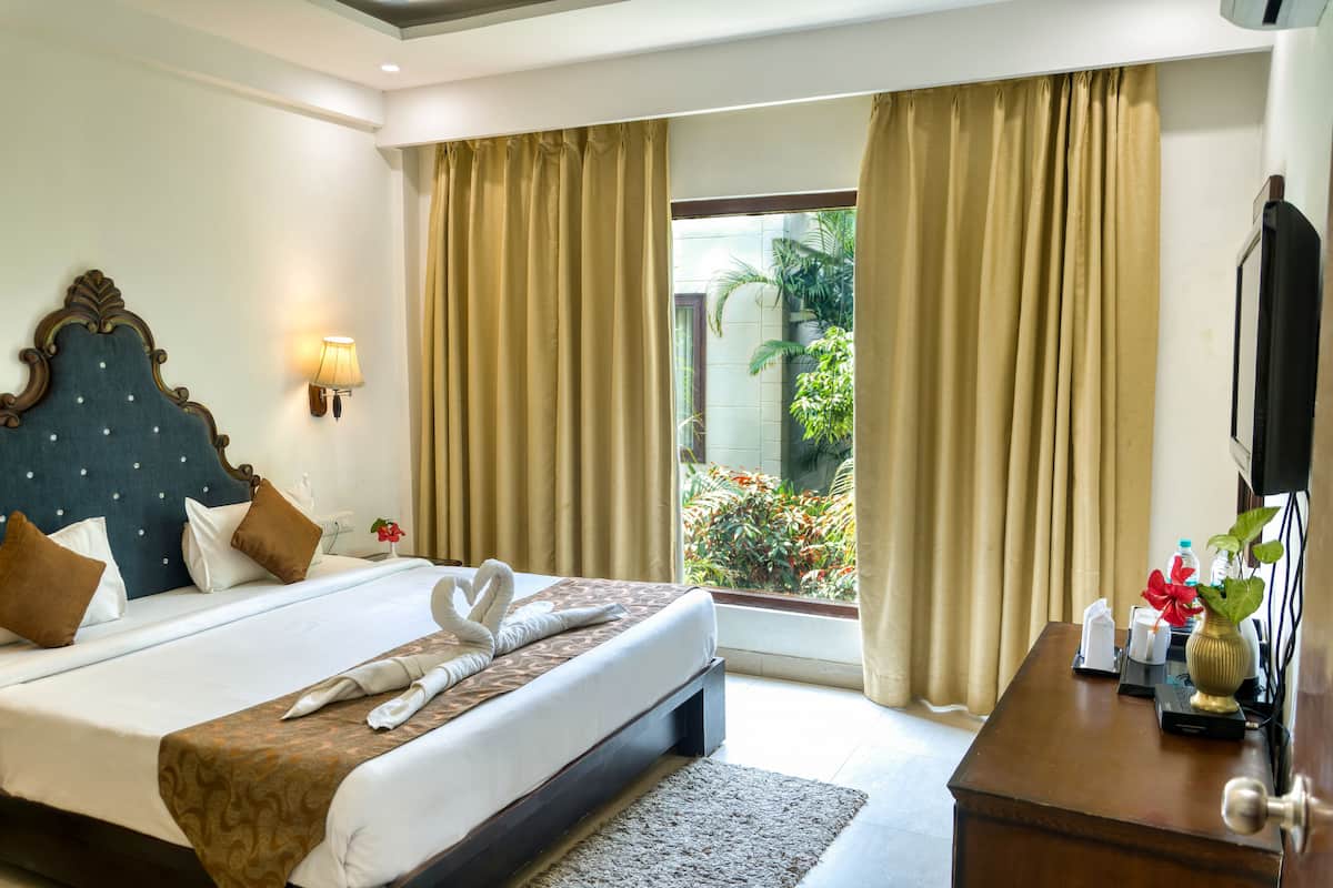 A hotel room with a large bed, a bedside table, a TV, and a view of the outdoors.