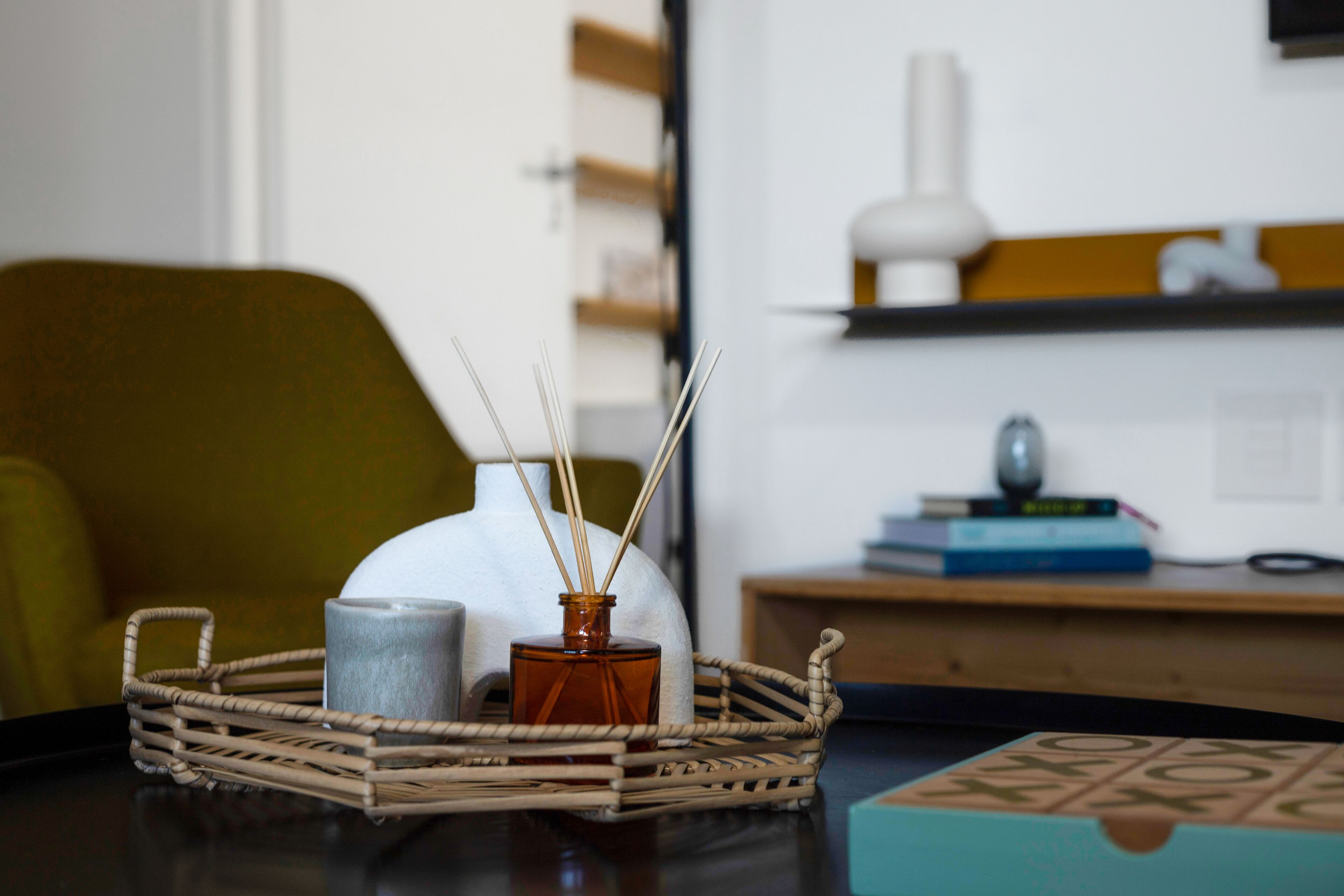 A wicker tray with a candle, a diffuser, and a box on a table.