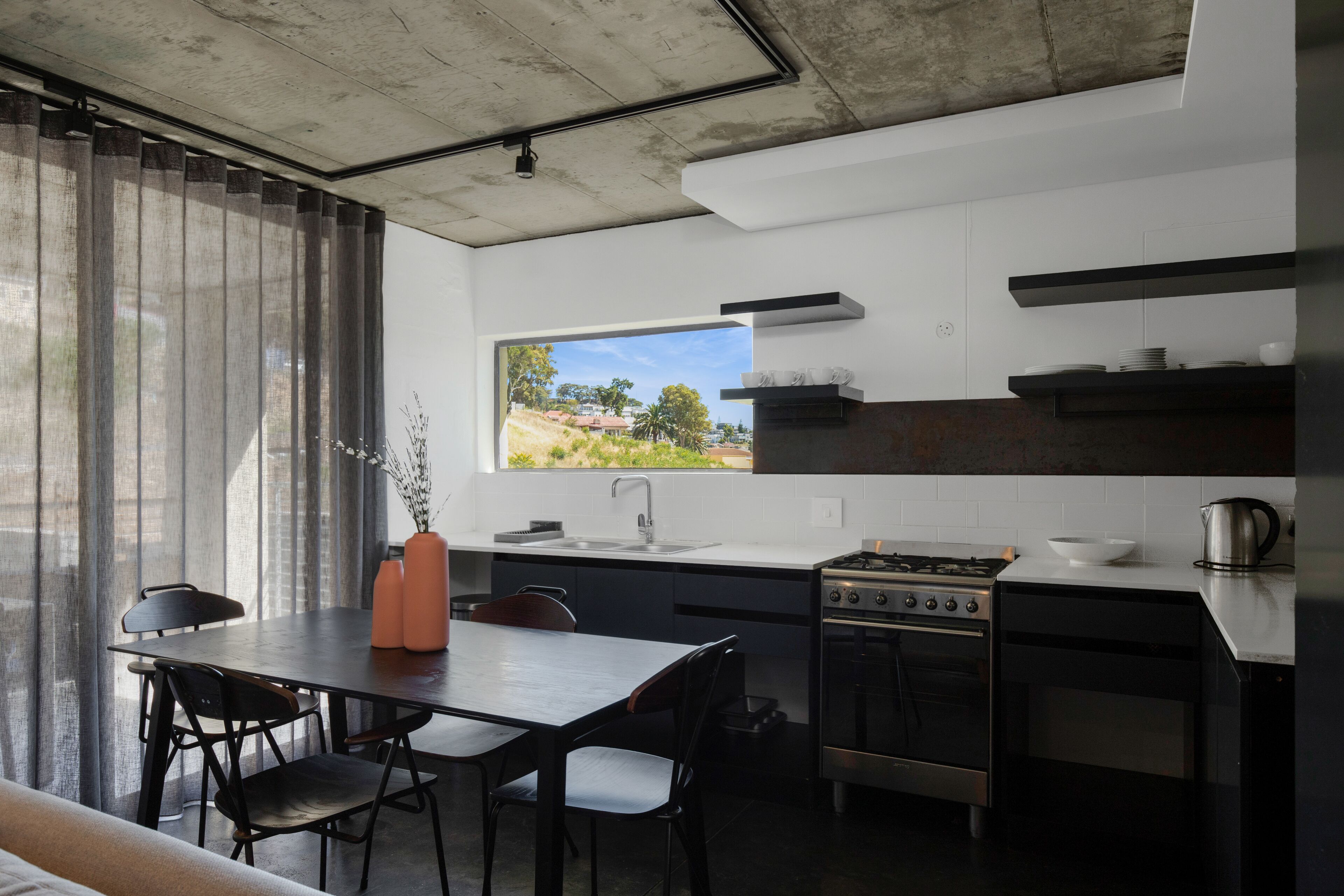 A modern kitchen with a dining area, featuring a large window, stainless steel appliances, and a minimalist design.