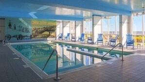 An indoor swimming pool with clear blue water, surrounded by lounge chairs and a mural depicting a coastal scene. - Studio unit at Boardwalk Villas  (Virginia Beach)
