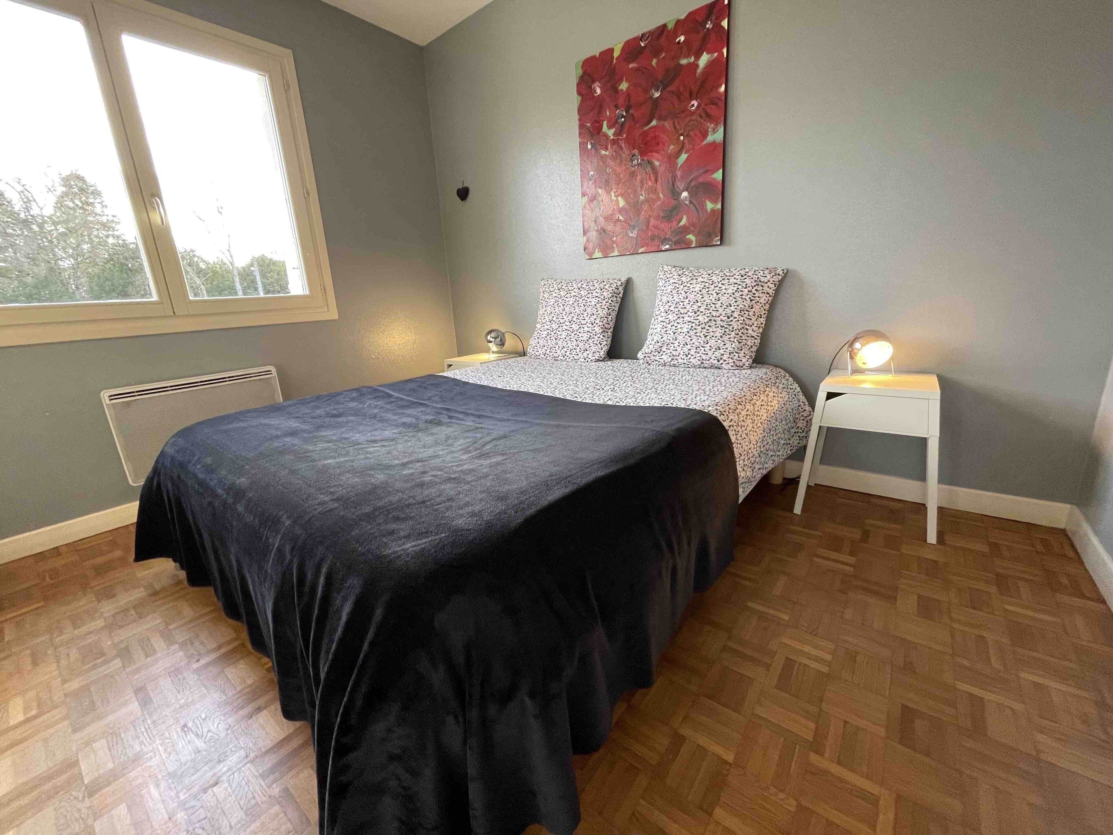 A bedroom with a bed, two bedside tables, a radiator, and a window.