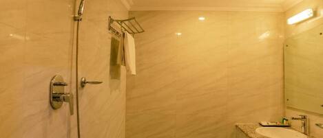 A modern bathroom with a marble wall, a shower, a sink, and a mirror.