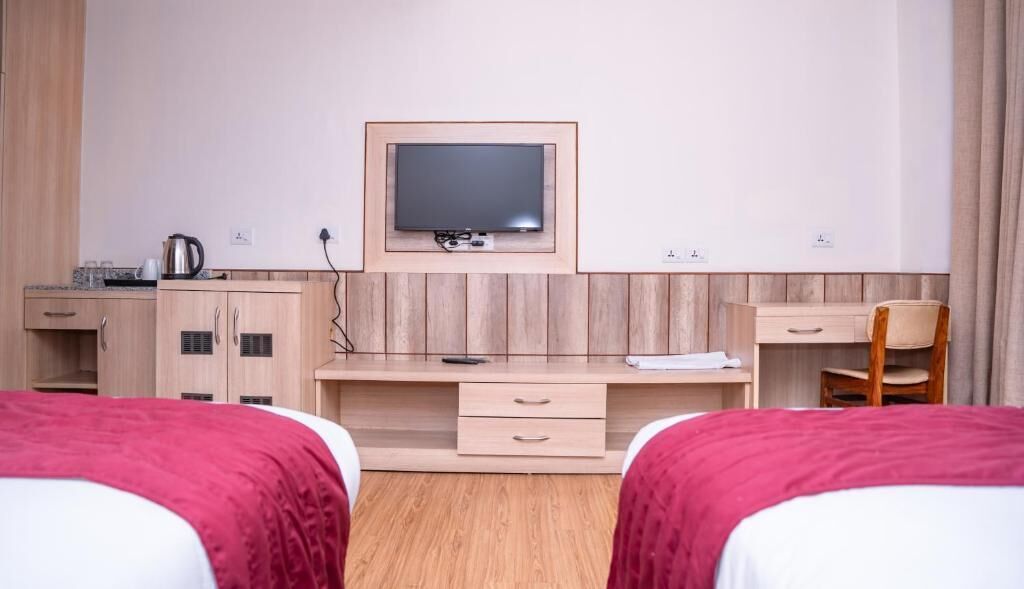 A hotel room with two beds, a desk with a television, a chair, and a small kitchenette.