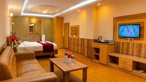 Una habitación de hotel con cama, sofá, televisión, una mesita con botellas de agua y un armario de madera.
