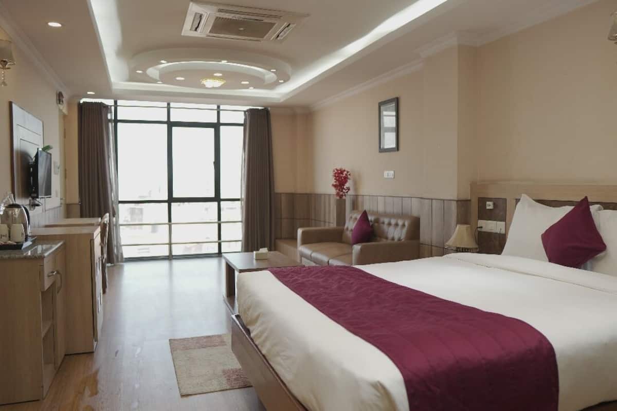 Een hotelkamer met een groot bed, een bureau met stoel, een televisie en uitzicht op de stad door grote ramen.