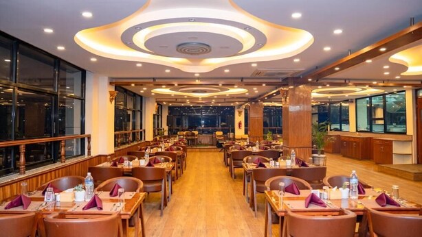 Un restaurante espacioso con numerosas mesas y sillas, una zona de bar central y grandes ventanales a lo largo de las paredes.