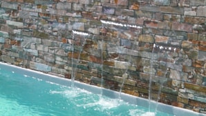 A swimming pool with a stone wall and water cascading down. - Gîte 2-***heated pool, Wifi, 2 bedrooms, air-conditioned, 1min river, 7min beach (Galéria)
