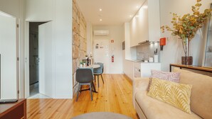 Eine moderne Wohnung mit Holzboden, einem Essbereich mit Tisch und Stühlen, einer Küche mit Herd und Spüle sowie einem Wohnbereich mit Sofa und Zimmerpflanze.