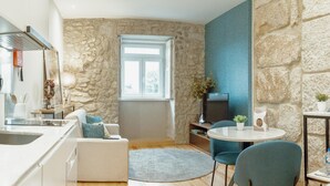 Ein modernes Wohnzimmer mit Steinwand, einem großen Fenster, einem Fernseher, einem runden Tisch und blauen Stühlen.