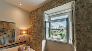 Ein Zimmer mit Steinwand, Fenster mit freiem Ausblick, einer Lampe und einem Bild an der Wand.
