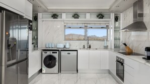 A modern kitchen with a built-in washer and dryer, a large window with a view of a mountain, and a stainless steel range hood. - Knightsbridge E906 (Cape Town)
