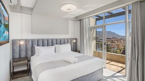 A modern hotel room with a large bed, a nightstand, a window with a view of the city, and a ceiling light. - Knightsbridge E906 (Cape Town)