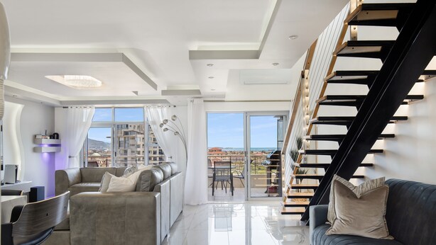 A modern living room with a sofa, a dark-colored couch, and a staircase with a unique design. - Knightsbridge E906 (Cape Town)