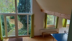 A room with large windows, a bench, and a ping pong table. - Vacation cottage Haus Hellhake (Sundern (Sauerland))