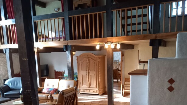 A spacious room with a high ceiling, wooden beams, a large wardrobe, a dining table with chairs, and a television. - Vacation cottage Haus Hellhake (Sundern (Sauerland))