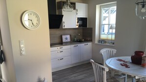 Una cocina con armarios blancos, un microondas, un reloj y una mesa de comedor con sillas.