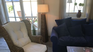 Una sala de estar con una silla de mimbre, un sofá azul, una lámpara y un jarrón con flores en un alféizar.