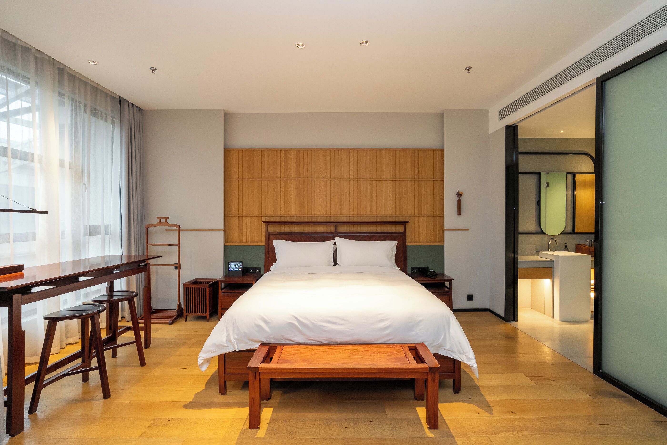 Una camera d'albergo moderna con un letto grande, una testiera in legno, una scrivania con degli sgabelli e vista sul bagno.