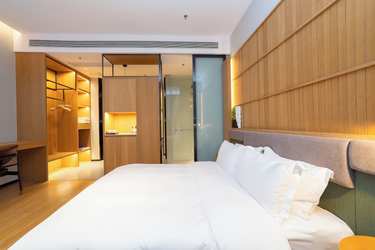 A modern hotel room with a large bed, wooden wardrobe, and a glass door leading to a bathroom.