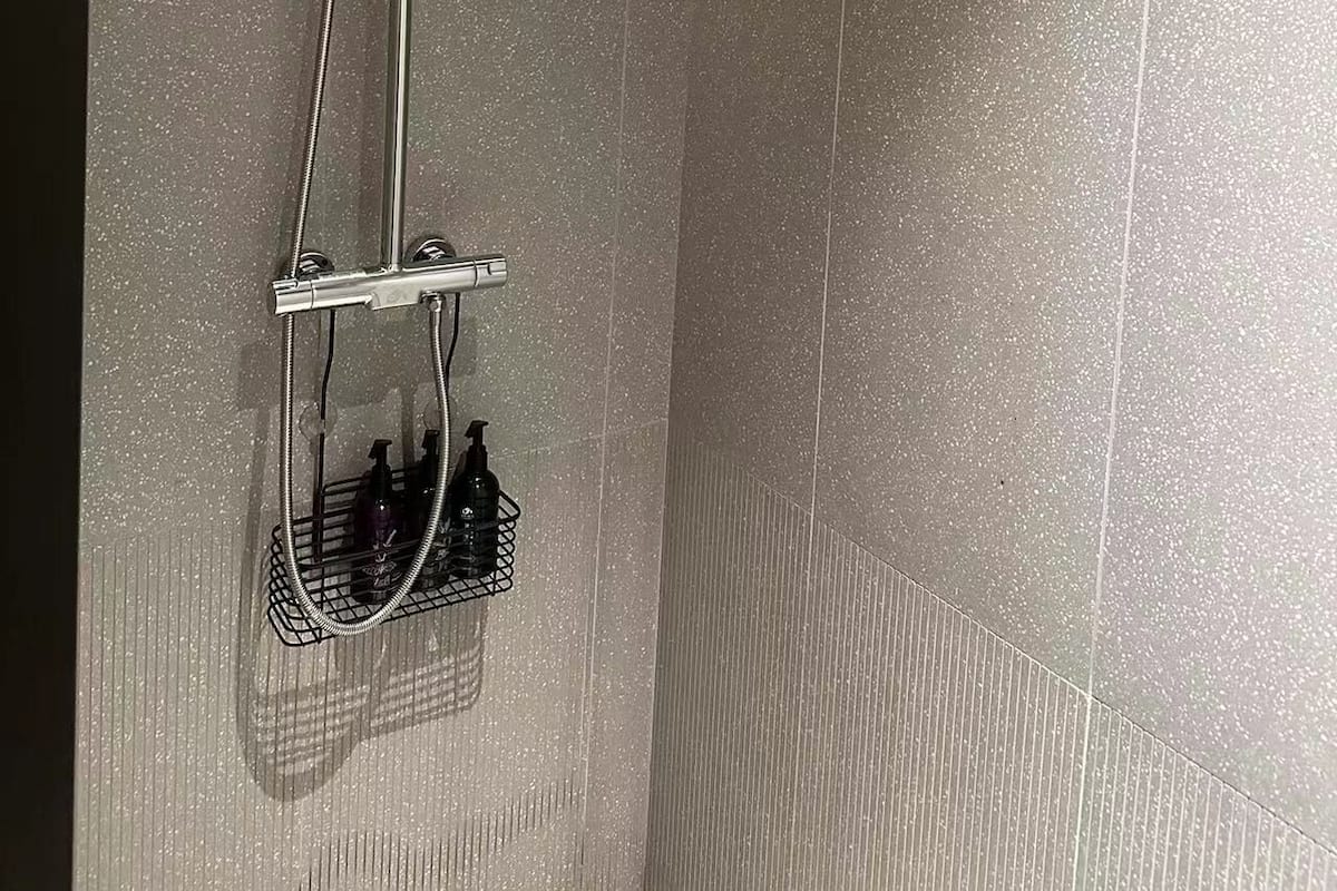 A shower with a handheld showerhead and a fixed showerhead, mounted on a wall with speckled tiles.
