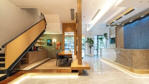A modern hotel lobby with a wooden reception desk, a seating area with a table and chairs, and a staircase leading to an upper floor. - Yitel Hotel Shanghai ex Timeless Boutique House (Shanghai)